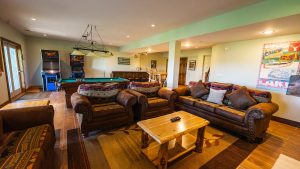 Relaxed game room with a pool table, leather sofas, and arcade machines against a green walls backdrop.