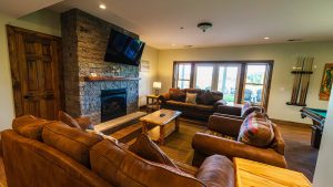 Cozy living room with a stone fireplace, mounted TV, and brown leather couches around a wooden coffee table.