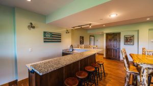 Kitchen bar area with granite countertop, dark wood cabinets, and wooden bar stools along a long island; turquoise walls and a doorway with a framed poster nearby.