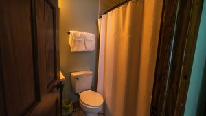 Small bathroom with a white toilet, beige shower curtain, and a towel rack mounted on the wall above the toilet.