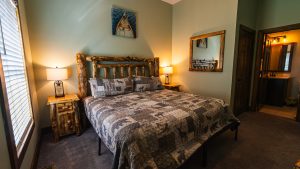 Rustic bedroom with a log bed, twin log nightstands, warm lamps, and a window with blinds.