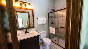 Modern bathroom with dark wood vanity, framed mirror, and a glass shower; towels on rack and warm lighting above mirror.