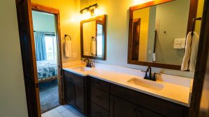 Bathroom with a double-sink vanity, dark wood cabinets, and three framed mirrors above a marble countertop with warm lighting.