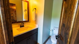 Small bathroom with a dark wood vanity, yellow-lit mirror, white towels on a ring, and a toilet nearby.