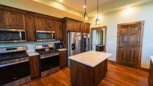 Kitchen with dark wood cabinets, stainless steel appliances, and a marble-topped island; warm pendant lights and wood floors.
