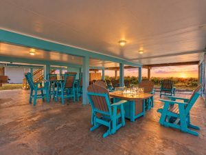 Turquoise Adirondack chairs and tables around a fire pit on a covered patio at sunset, coastal vibe and outdoor seating