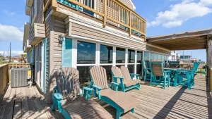Coastal house with large windows and turquoise outdoor chairs on a wooden deck at the beach