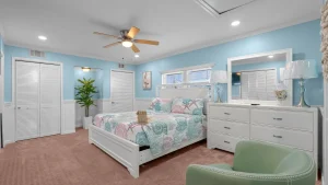 Coastal-style bedroom with blue walls, white furniture, and a bed with a pastel shell-pattern quilt.
