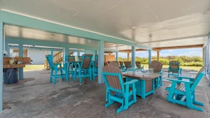 Outdoor covered patio with bright turquoise chairs and brown Adirondack seats around tables under a light concrete ceiling