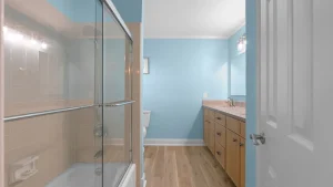 Bathroom with a glass shower enclosure on the left, beige tiled walls, blue walls, and a light wood vanity with a sink on the right.