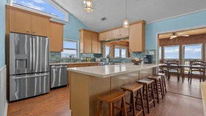 Modern kitchen with stainless steel fridge, light wood cabinets, blue walls, and a breakfast island with wooden stools.