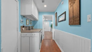 Bright laundry room with white cabinets, blue walls, granite counter, and front-loading washer/dryer under the counter. Decorative jars on the counter add a homey touch.
