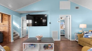 Living room with a wall-mounted flat-screen TV on blue walls and a wooden coffee table in the foreground.