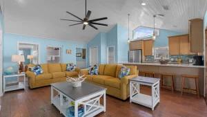 Open-concept living room and kitchen with blue walls, a mustard-yellow sectional sofa, hardwood floors, and a ceiling fan centerpiece.