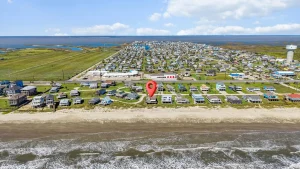Aerial view of a coastal town with a grid of houses along the beach and a red location pin in the foreground.