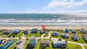 Aerial view of a beachside neighborhood with colorful houses and a red location pin near the shore.